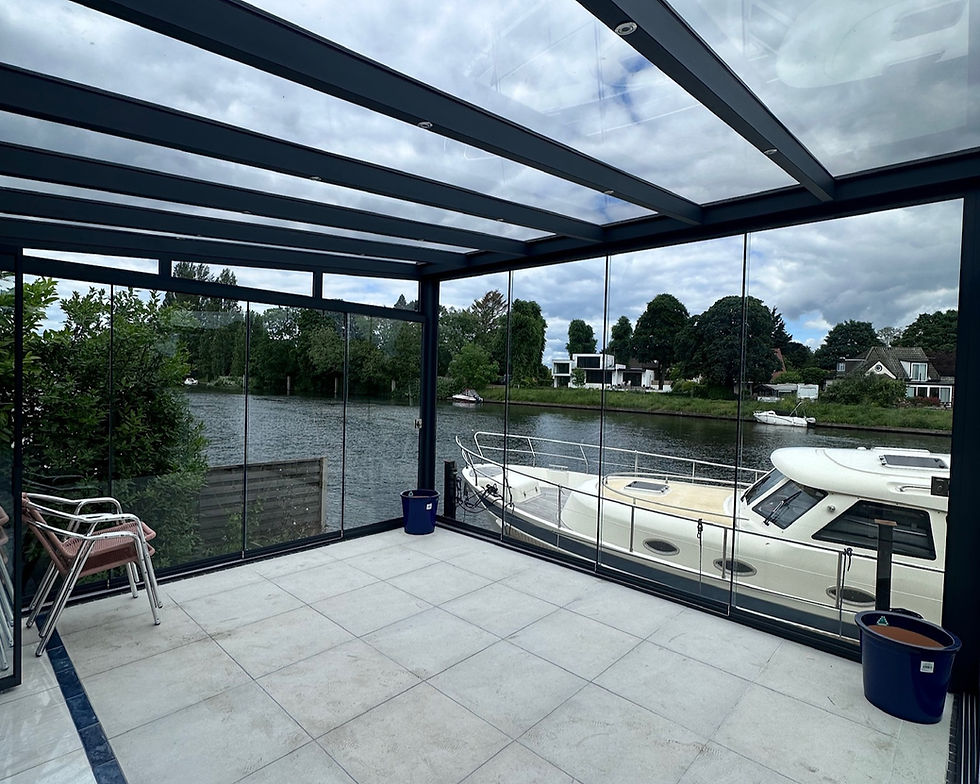 Anthracite grey framed glass room veranda with glass sliding doors and LED spot lights, free-standing as an outdoor living area, overlooking the river.