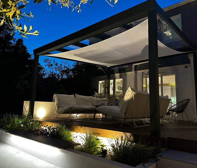 Jet black aluminium pergola with glass roof and shade sail, featuring garden sofa chairs, designed as an outdoor lounge. Installed in Marlow, Buckinghamshire.