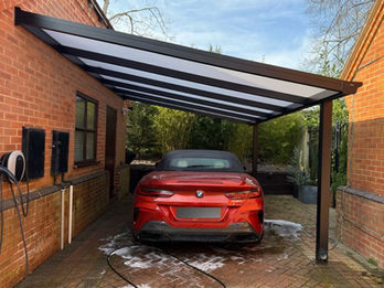 Black carport frame with polycarbonate roof, covering a red BMW vehicle