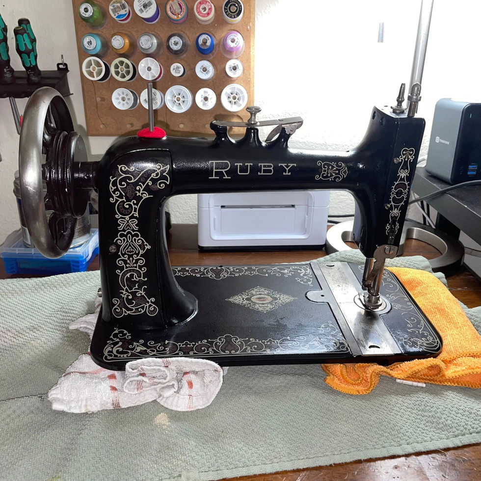 Restored vintage Ruby sewing machine with ornate silver decals, cleaned and detailed for display on a workbench with thread spools in the background