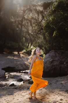 Woman in orange dress twirls on beach, YapingLiuPhotography, next to trees.