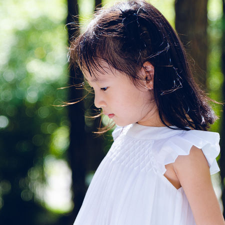Young girl in white dress, outdoors looking down at something. YapingLiuPhotography