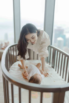 A smiling mother leans over a baby in a crib. YapingLiuPhotography