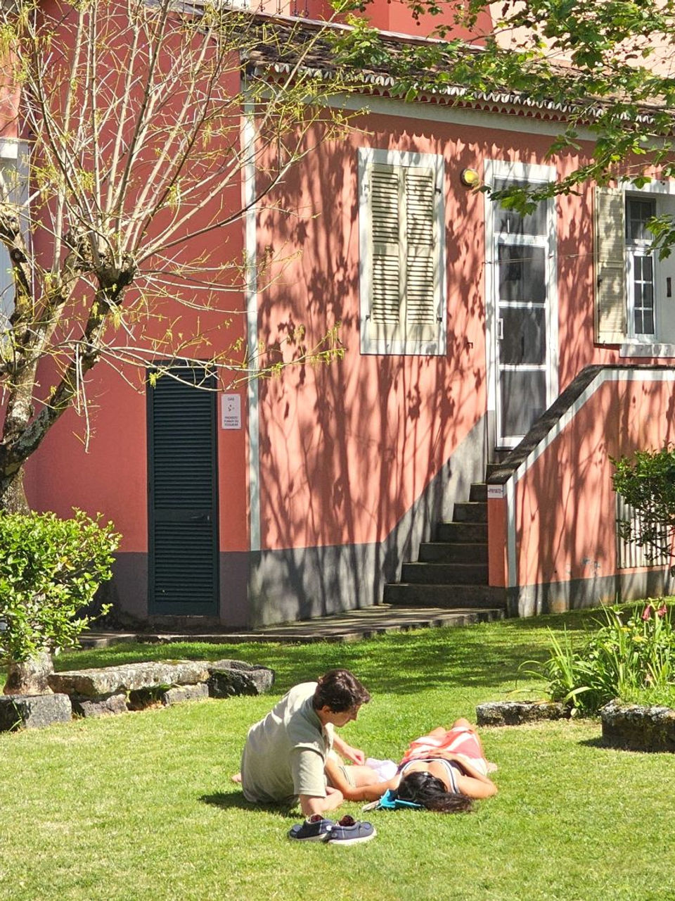 Guests relaxing on the lawn in front of the Garden Rooms at Solar de Lalem, surrounded by vibrant greenery, flowering plants, and the historic pink facade of the estate.