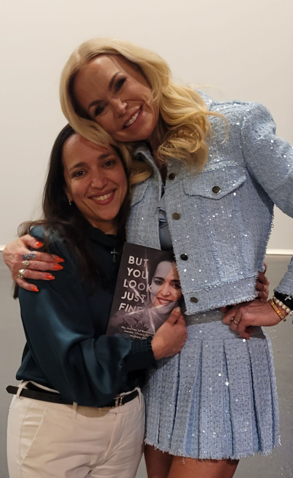 Michele Roys holding her book - But You Look Just Fine, while hugging Amberly Lago at the Unstoppable Summit Event