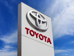 Sign featuring the Toyota logo and text against a bright blue sky with scattered clouds, creating a bold and vibrant scene.
