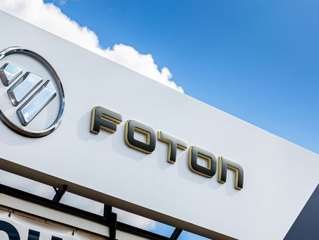 Foton logo on a white sign against a blue sky with clouds.