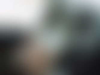 Hands holding a phone while driving, inside a car with a steering wheel visible. Sunlight casts a shadow, implying a casual setting.