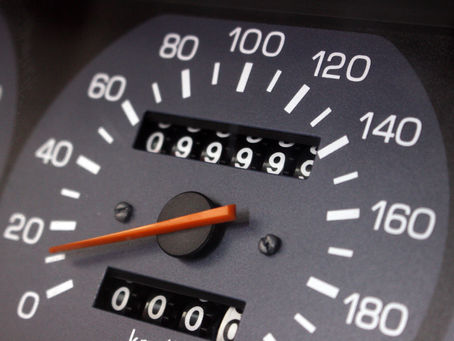Close-up of a car speedometer with an orange needle pointing at 20. Odometer reads 99999, suggesting the vehicle is near a milestone.