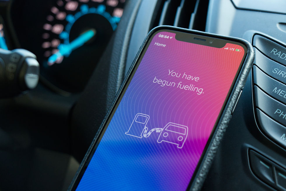 Smartphone in car displaying "You have begun fuelling" on a gradient screen. Blurred car dashboard in background with blue gauges.