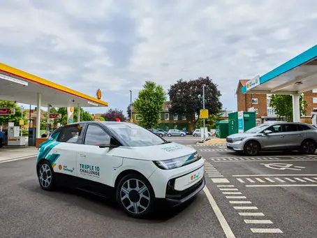 Two electric cars at a Shell Recharge station, one marked TRIPLE 10 CHALLENGE, under a cloudy sky.