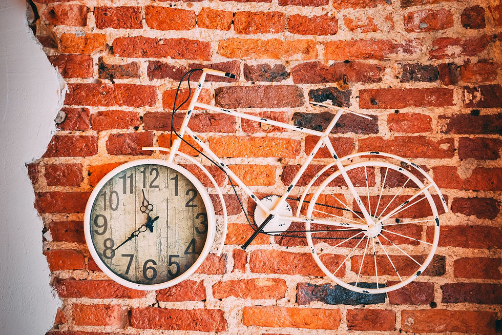 A vintage-style wall clock integrated into a metal bicycle frame on an exposed brick wall.