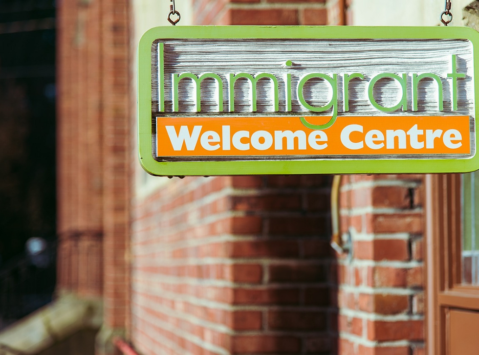 A green and orange sign reads "Immigrant Welcome Centre" against a red brick wall.