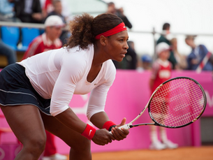 File photo of tennis player Serena Williams in a ready position during a Fed Cup 2012 match. She is wearing a white top, a black skort with white piping, along with red arm and head bands while holding her racket. 