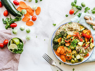 Flat-lay table photography of colorful vegetables and lime slices surrounding a bowl of quinoa, carrots, broccoli, zucchini, tomatoes, brussel sprouts, ginger root, and herbs by Ella Olsson on Pexels. 