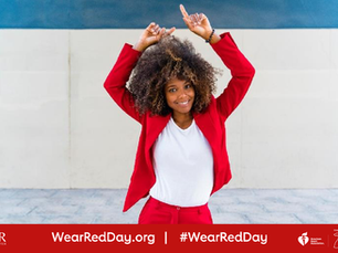 Woman in a white top and red suit smiles and points up against an urban setting. Text on the red background says: "WearRedDay.org" and "#WearRedDay."