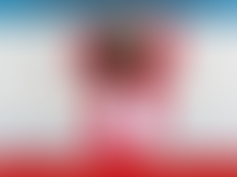 Woman in a white top and red suit smiles and points up against an urban setting. Text on the red background says: "WearRedDay.org" and "#WearRedDay."