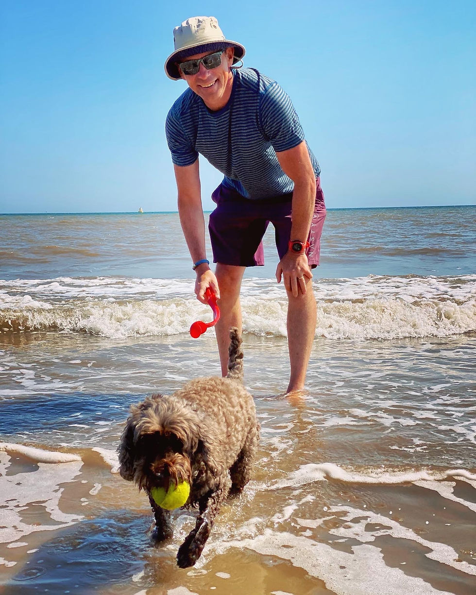 Man paddling in sea with cock-a-poo dog