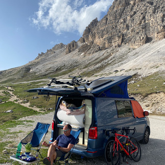 man sitting next to blue VW camper in the mountains