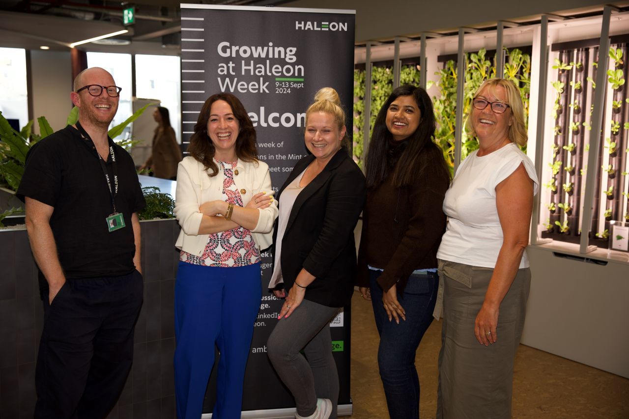 Five members of the event team smiling in front of the Growing at Haleon Week welcome banner