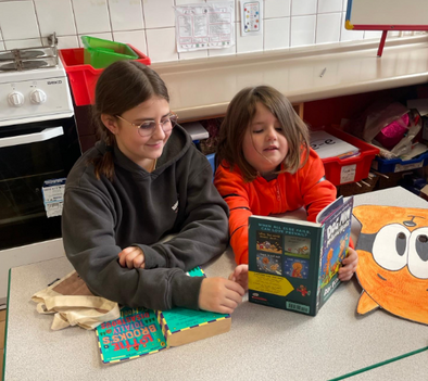 Two students reading together, one holds a 'Dog Man' book