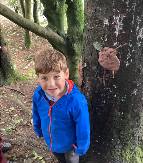Smiling young boy in blue jacket stands by tree with art.