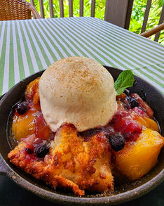 A cast iron skillet full of peach berry cobbler with a scoop of vanilla ice cream