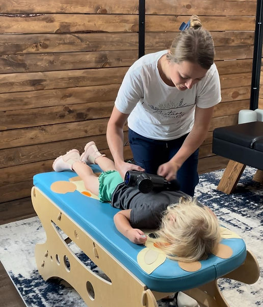 Chiropractor using percussion therapy during a child’s visit