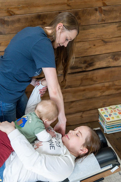 Chiropractor providing a postpartum adjustment while a mother holds her infant