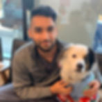 A veterinarian with dark hair and a beard sits in the animal hospital hugs a white dog with gray ears.