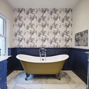 Elegant traditional bathroom featuring a freestanding bath, navy blue panelling, floral wallpaper and marble flooring.

