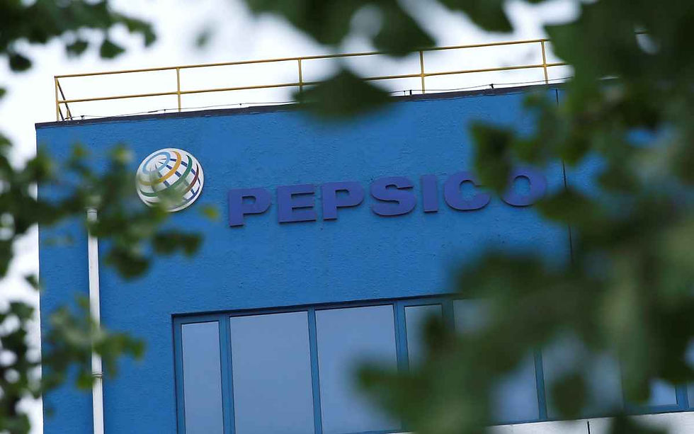 Logotipo azul de la corporación PepsiCo visible en la fachada superior de su edificio de oficinas, visto a través de ramas de árboles desenfocadas en primer plano.