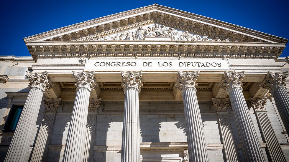 "Vista contrapicada de la fachada principal del Congreso de los Diputados en Madrid, destacando las columnas corintias y el letrero bajo el frontispicio."