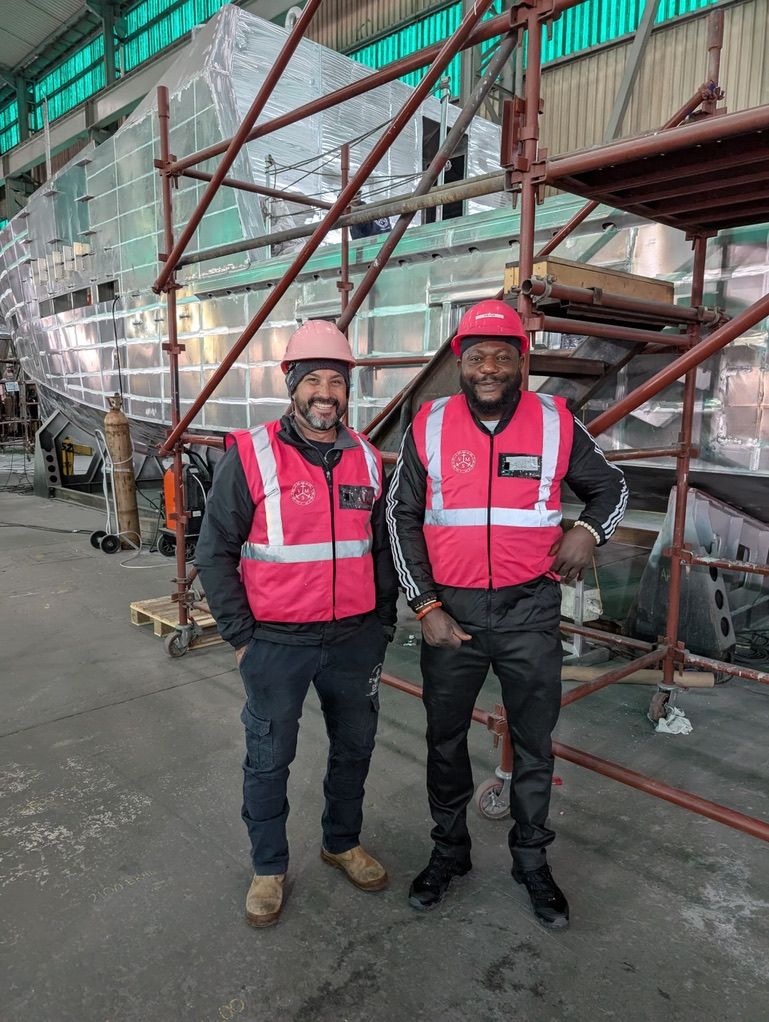 Steve and a client in hi-vis beside an aluminium hull under construction