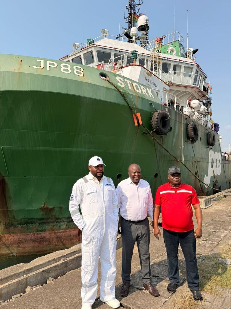 Three men on the quay beside the green hull of JP88 Stork