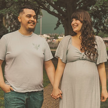 Man and pregnant woman holding hands and smiling in front of trees