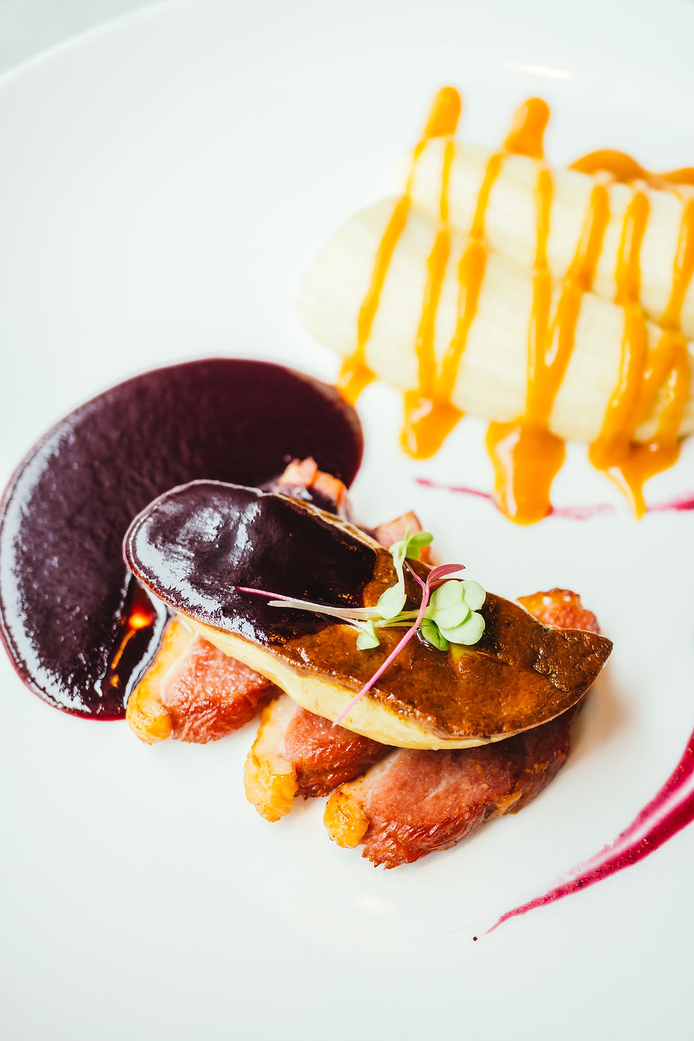 Foie gras mi-cuit au four sur lit de magret de canard avec sauce aux fruits rouges, accompagné de purée garnie de sauce à la carotte, dans une présentation gastronomique moderne.