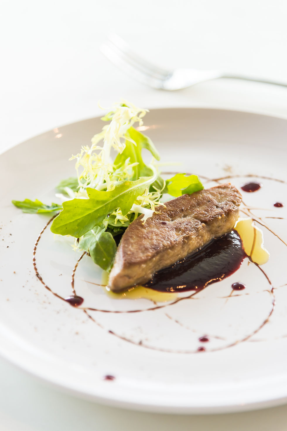 Foie gras mi-cuit au four présenté avec une salade verte fraîche et une sauce au vin rouge réduite, offrant une présentation gastronomique élégante sur une assiette blanche.