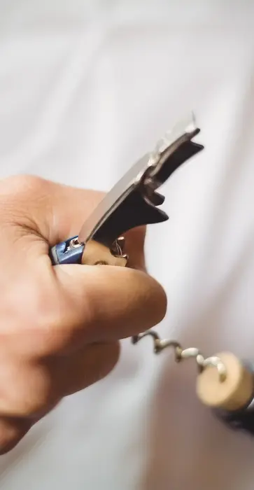 Hand opening a wine bottle with a corkscrew
