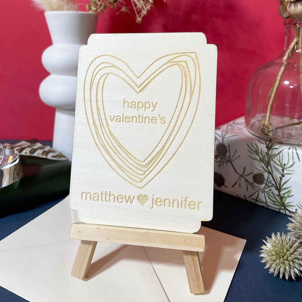 wooden card displayed on an easel with engraved hearts and names seperated by a  small heart