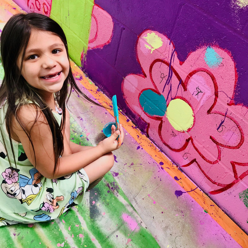 Smiling child painting a flower community mural led by artist and muralist Jaya King, Jaya’s Art in Sacramento.