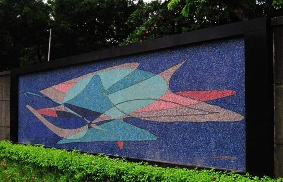 Eye-level view of a mosaic mural on an outdoor public wall showing abstract shapes and vibrant colors