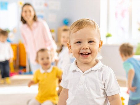 Boy smiling, with childminder with other children behind him