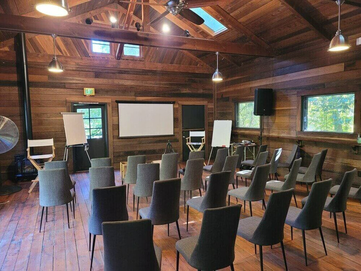 ustic wood-paneled meeting room at Dawn Ranch with rows of chairs, projection screen, and AV equipment — ideal for corporate offsite presentations and team workshops in Sonoma County