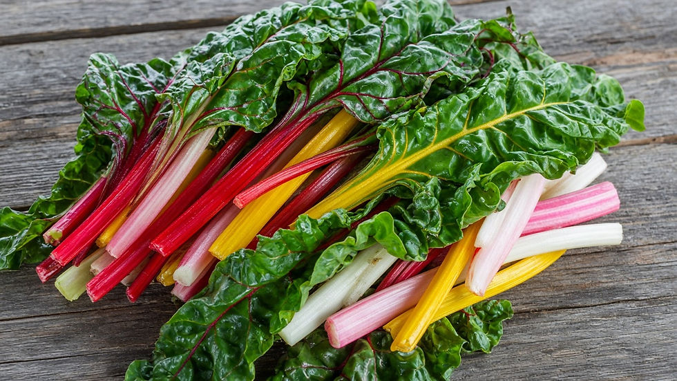 A bundle of freshly harvested rainbow Swiss chard with bright red, yellow, pink and white stems and glossy crinkled green leaves on a rustic wooden board