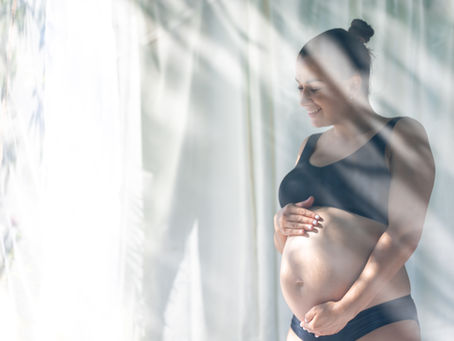 Mujer embarazada sonriendo de perfil mientras sostiene su vientre, iluminada por una luz natural suave, acompañada por el logotipo de Prenatal Life Test y la frase "Grandes alegrías".