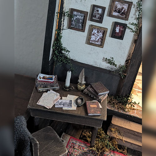 Détail de bureau miniature avec livres, lettres et objets anciens dans une scène poétique de valisette, création artistique Mihne Creations