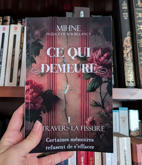 Livre Ce qui demeure – Tome 1 tenu devant une bibliothèque
