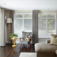 A traditional lounge with a wing back chair and three windows fitted with shutters