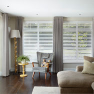 A traditional lounge with a wing back chair and three windows fitted with shutters